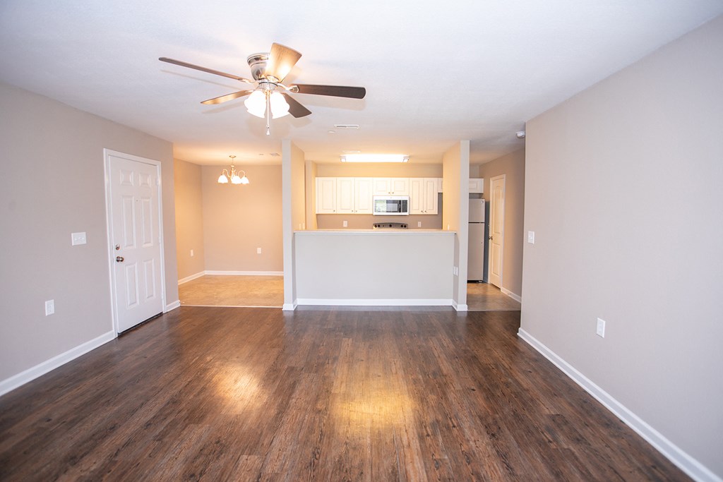 an empty living room with a ceiling fan and a kitchen