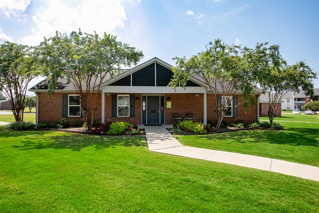 the front of a brick house with grass and trees
