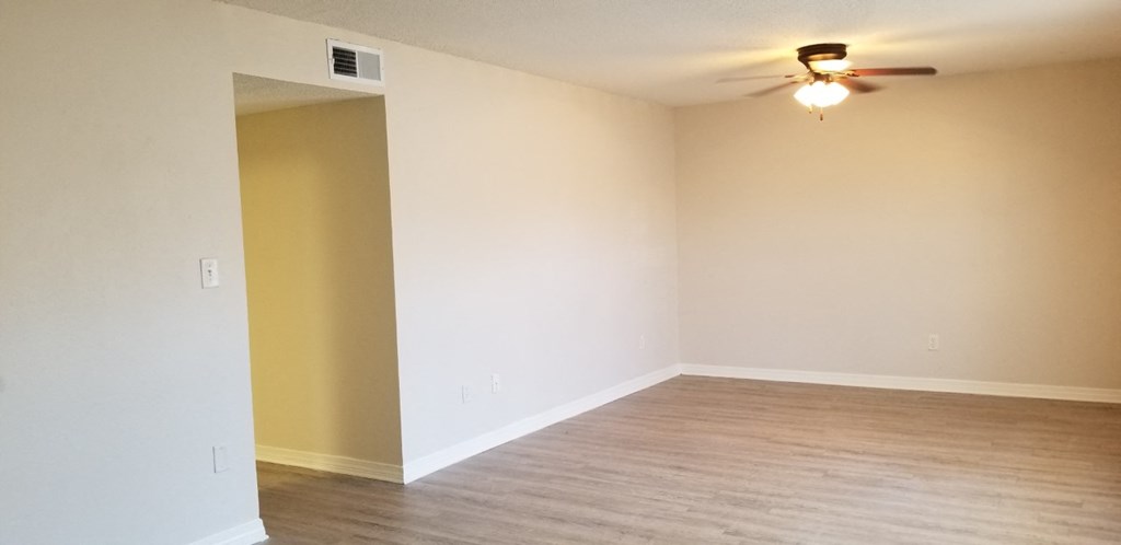 an empty living room with wood floors and a ceiling fan