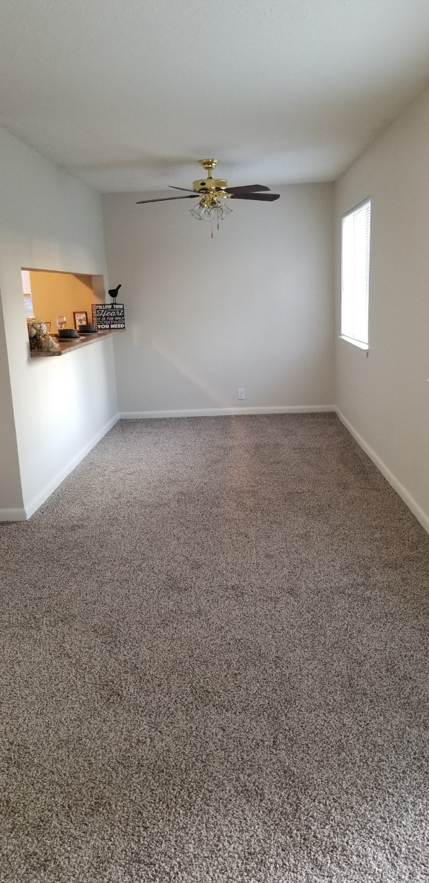 an empty living room with carpet and a ceiling fan