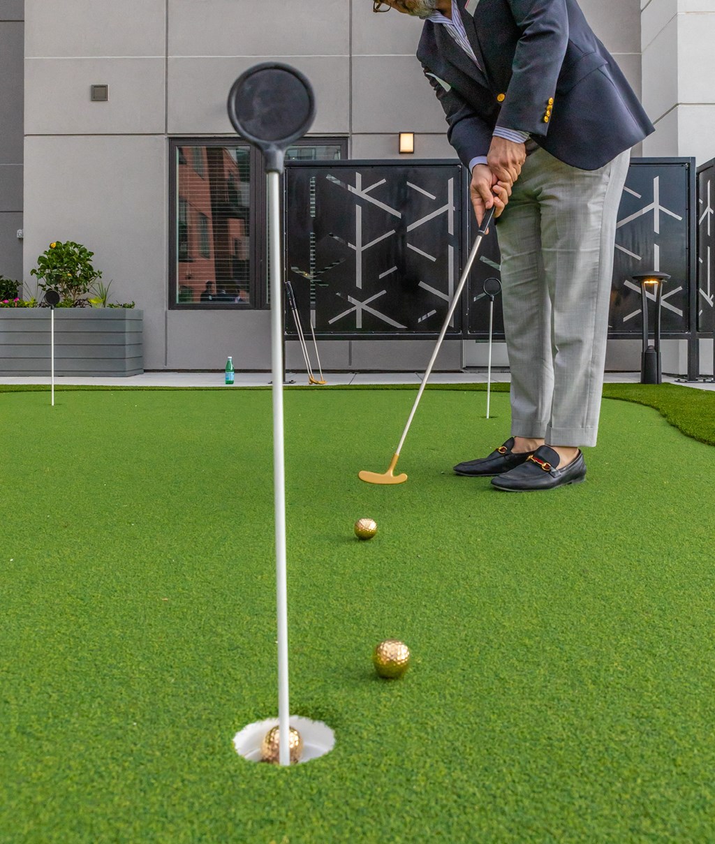 Man in a suit on a putting green about to hit the ball