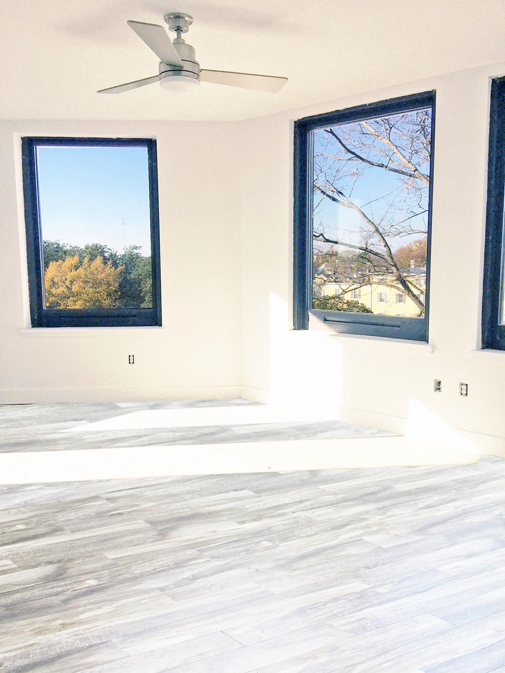 an empty room with a ceiling fan and two windows