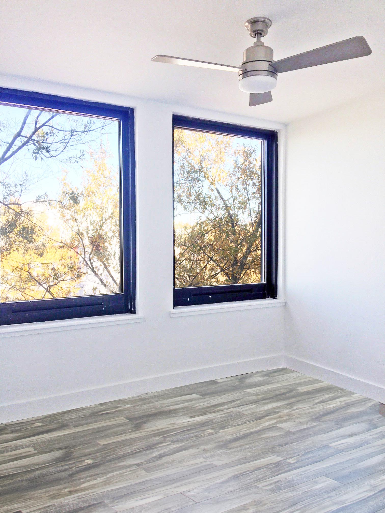 an empty room with two windows and a ceiling fan