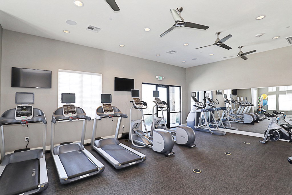 a gym with cardio machines and a tv