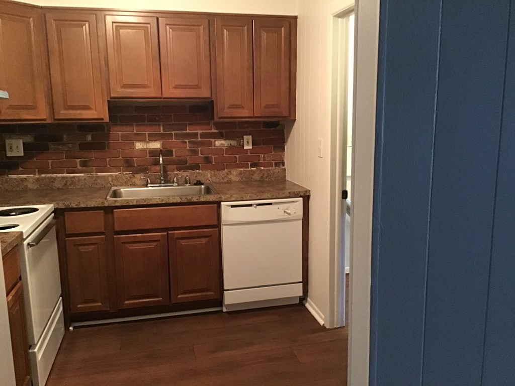 a kitchen with wooden cabinets and white appliances and a brick wall