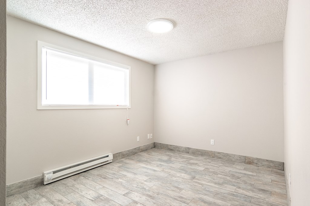 an empty room with a window and vinyl flooring