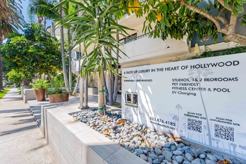 a sign in front of a building with palm trees and rocks