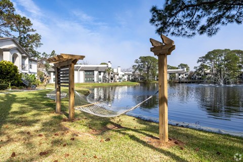 A wooden sculpture of a bird is perched on a pole next to a body of water.