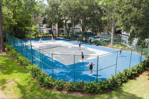 A tennis court surrounded by a green fence and trees.