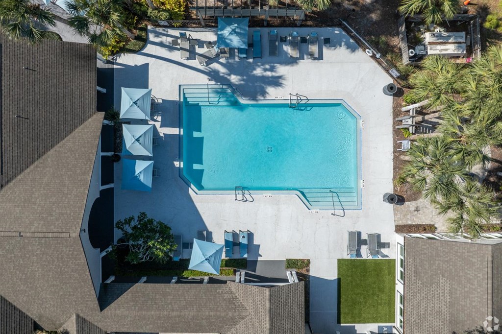 An aerial view of a swimming pool surrounded by palm trees and a white building.