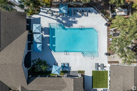 An aerial view of a swimming pool surrounded by palm trees and a white building.