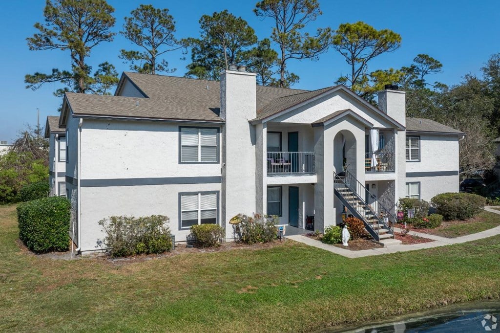 A white house with a grey roof and a balcony on the second floor.