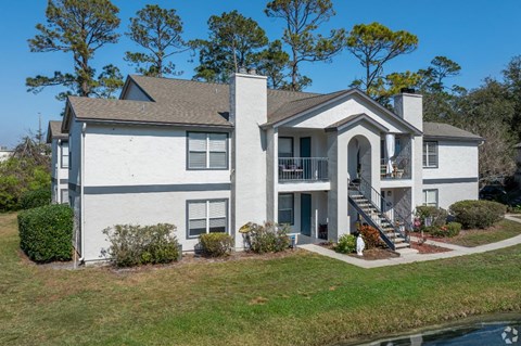 A white house with a grey roof and a balcony on the second floor.