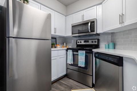 A kitchen with a stainless steel refrigerator and a microwave above the stove.