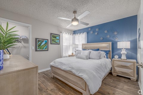 A bedroom with a bed, nightstand, and a plant.