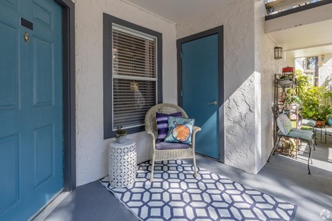 A blue door is on the left of a white wall with a chair and a pillow on the floor.