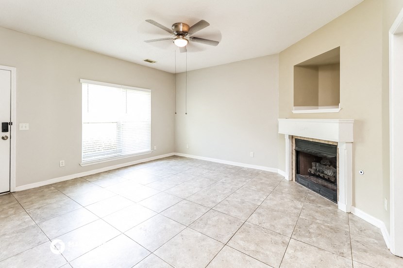 an empty living room with a fireplace and a ceiling fan