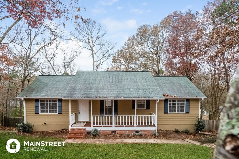 a small yellow house with a porch and a green roof