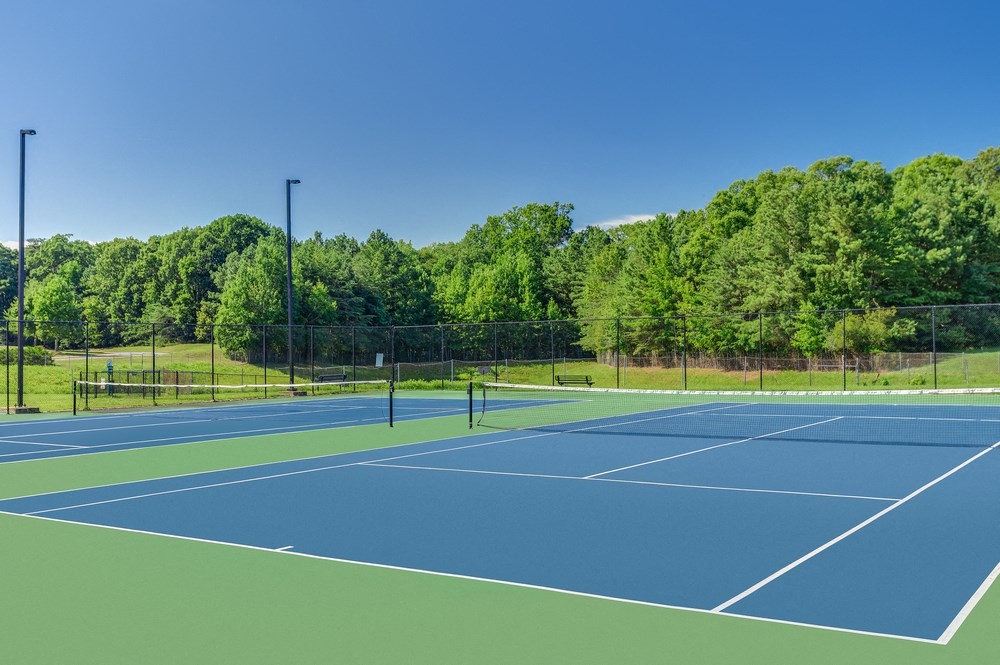two tennis courts with trees in the background on a sunny day