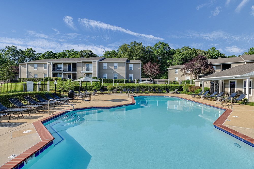 a swimming pool with chairs and umbrellas in front of apartment buildings