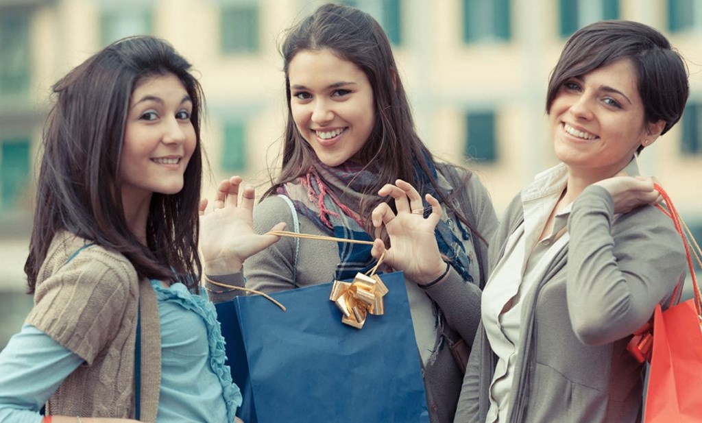 Three women are standing together and holding shopping bags.