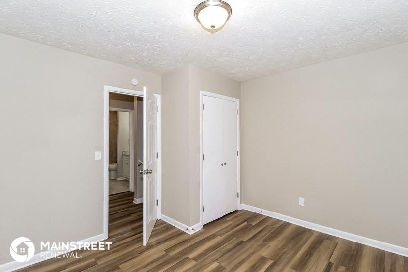 the living room of an apartment with wood flooring and a door to the bathroom