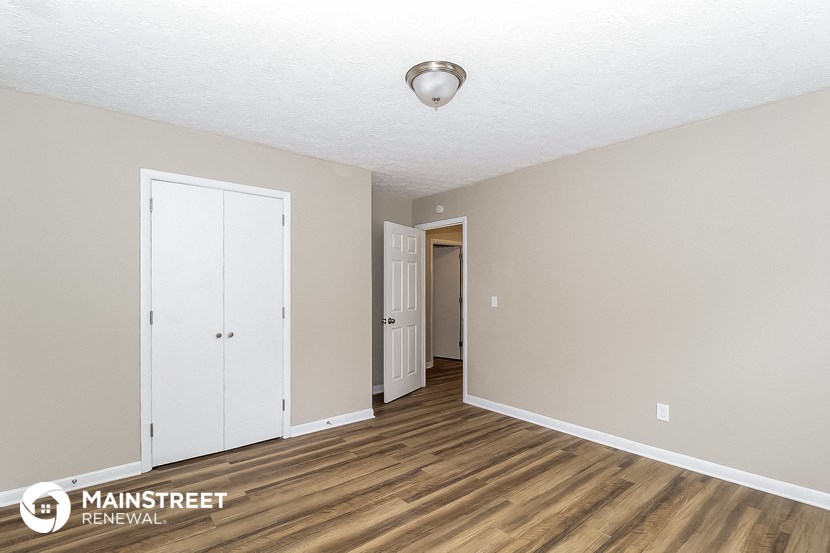 the living room of an apartment with wood flooring and a door to the hallway