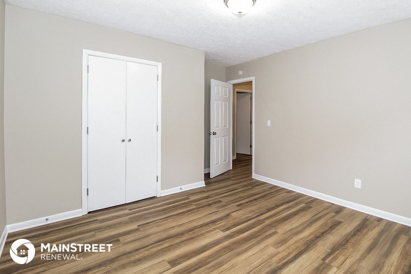 the living room of an apartment with wood flooring and white walls and doors