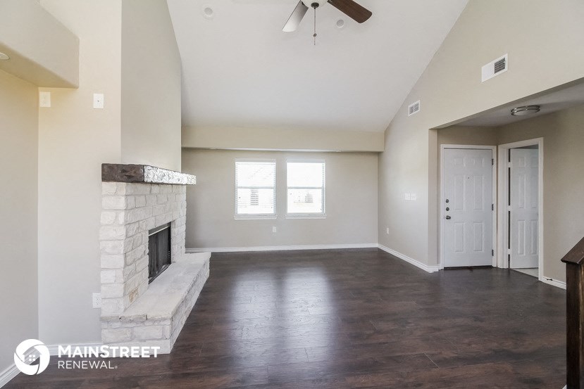 an empty living room with a stone fireplace and wood flooring
