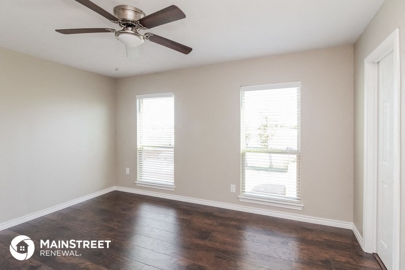 an empty room with a ceiling fan and two windows