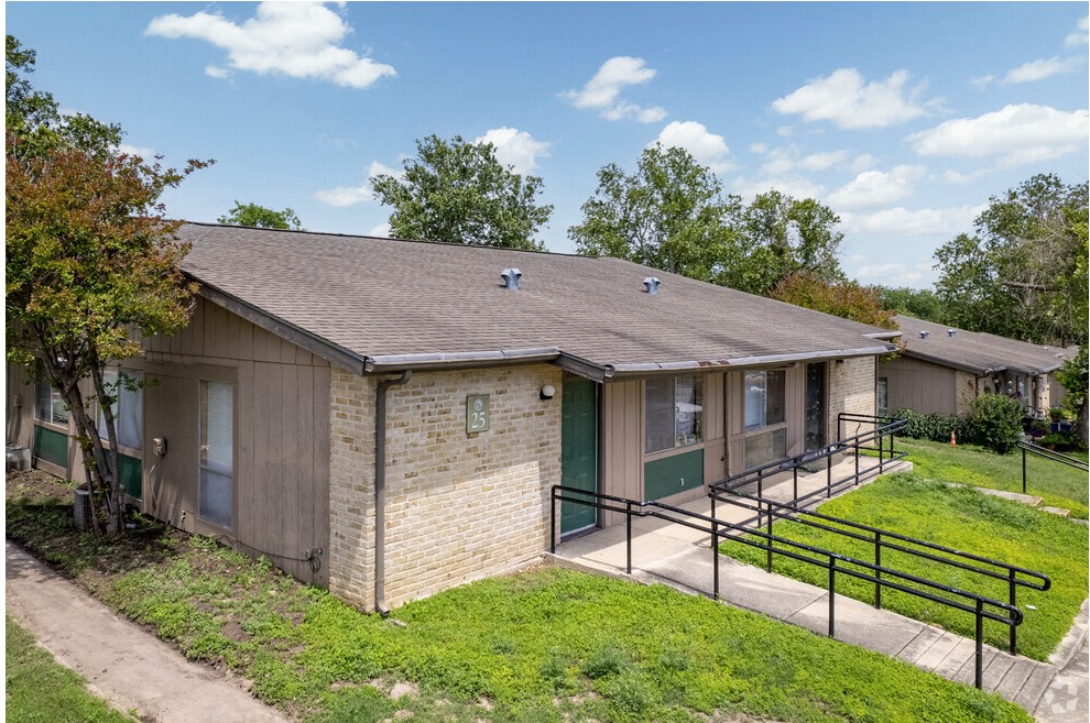 a brick building with green doors and a grassy yard