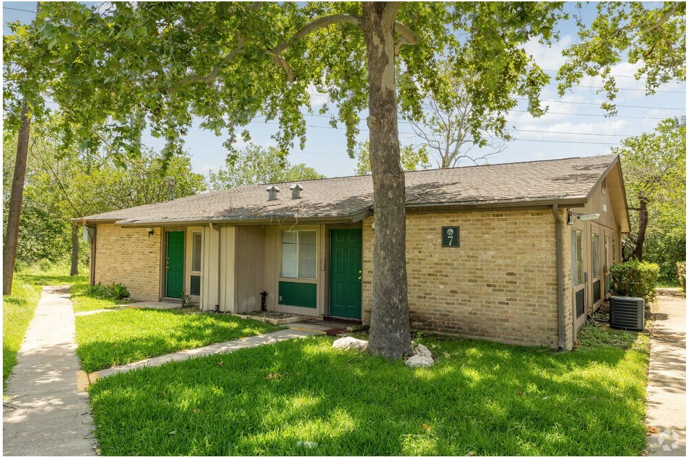 a small brick house with green doors and a tree