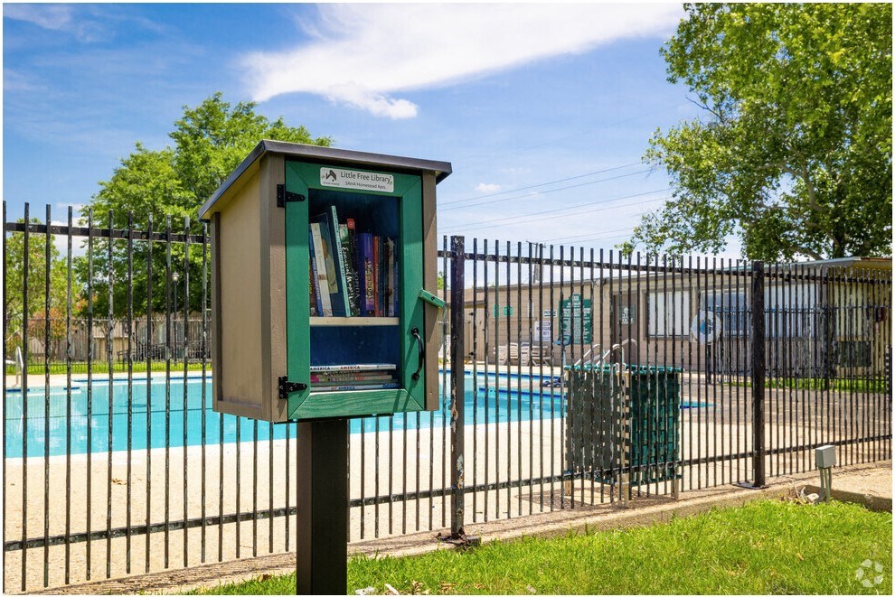a green mailbox with books in front of a swimming pool