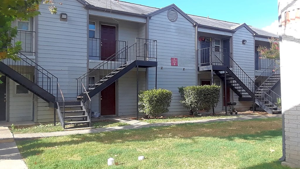 the front of an apartment building with stairs and a yard