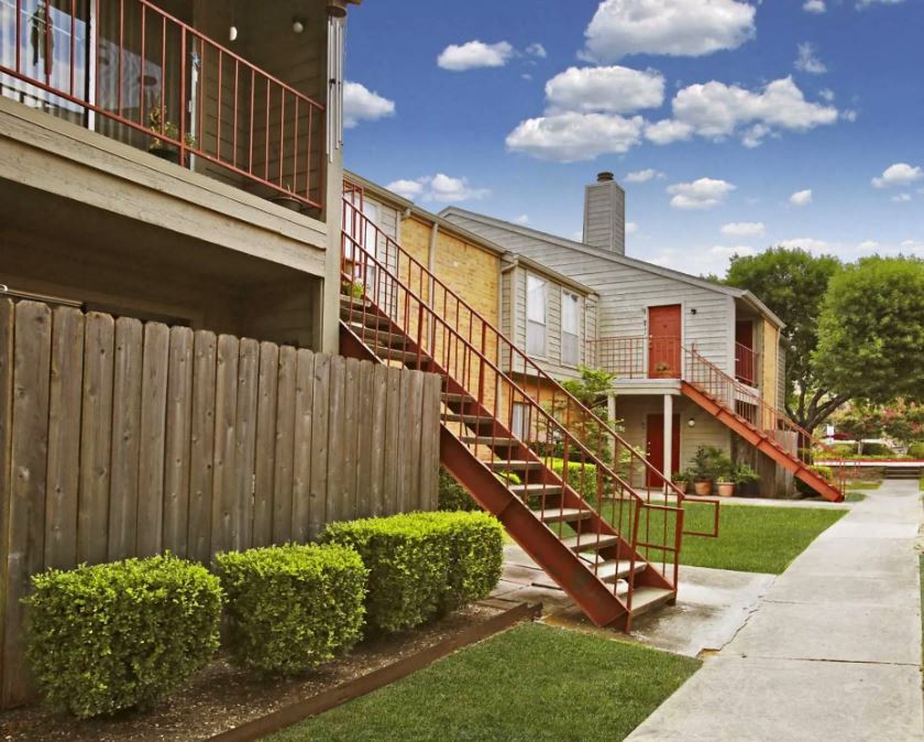apartment exterior with green shrubs, grey and red staircases leading to red front doors