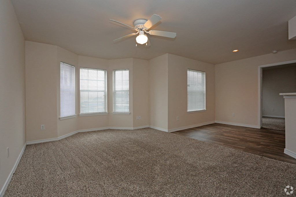 an empty living room with a ceiling fan and windows