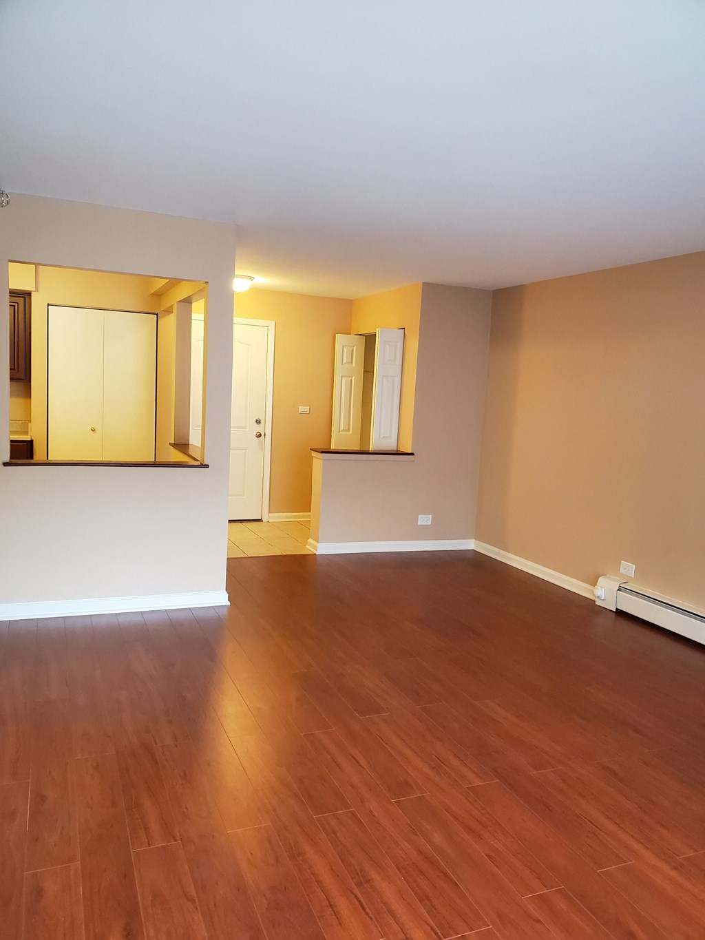 an empty living room with wood flooring and a kitchen