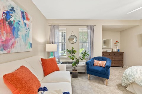 A living room with a white couch, a blue chair, and a painting on the wall.