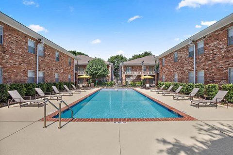 A swimming pool surrounded by lounge chairs in front of a brick building.