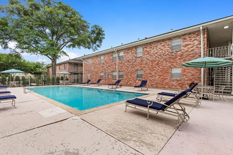 A pool area with sun loungers and a brick building in the background.