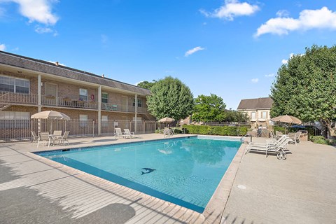 A large swimming pool is surrounded by lounge chairs and umbrellas.