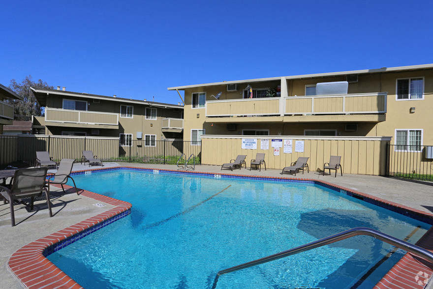 A swimming pool in front of a building with sun loungers around it.