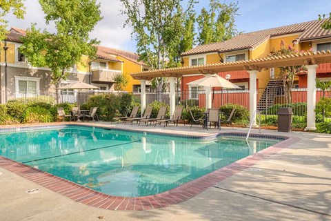 A swimming pool surrounded by a patio with chairs and umbrellas.