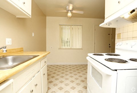 A kitchen with a white stove top oven and a white tiled floor.