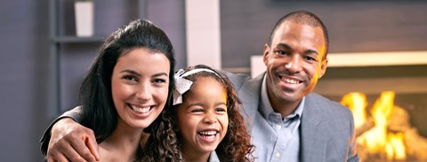 A family of three is smiling and posing together in front of a fireplace.