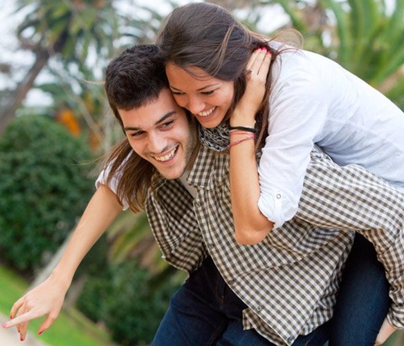 A man is carrying a woman on his back in a park.