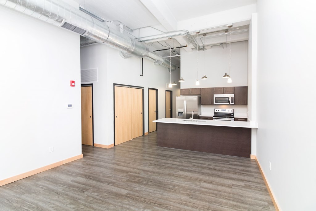 an empty room with a kitchen and white walls and wood floors