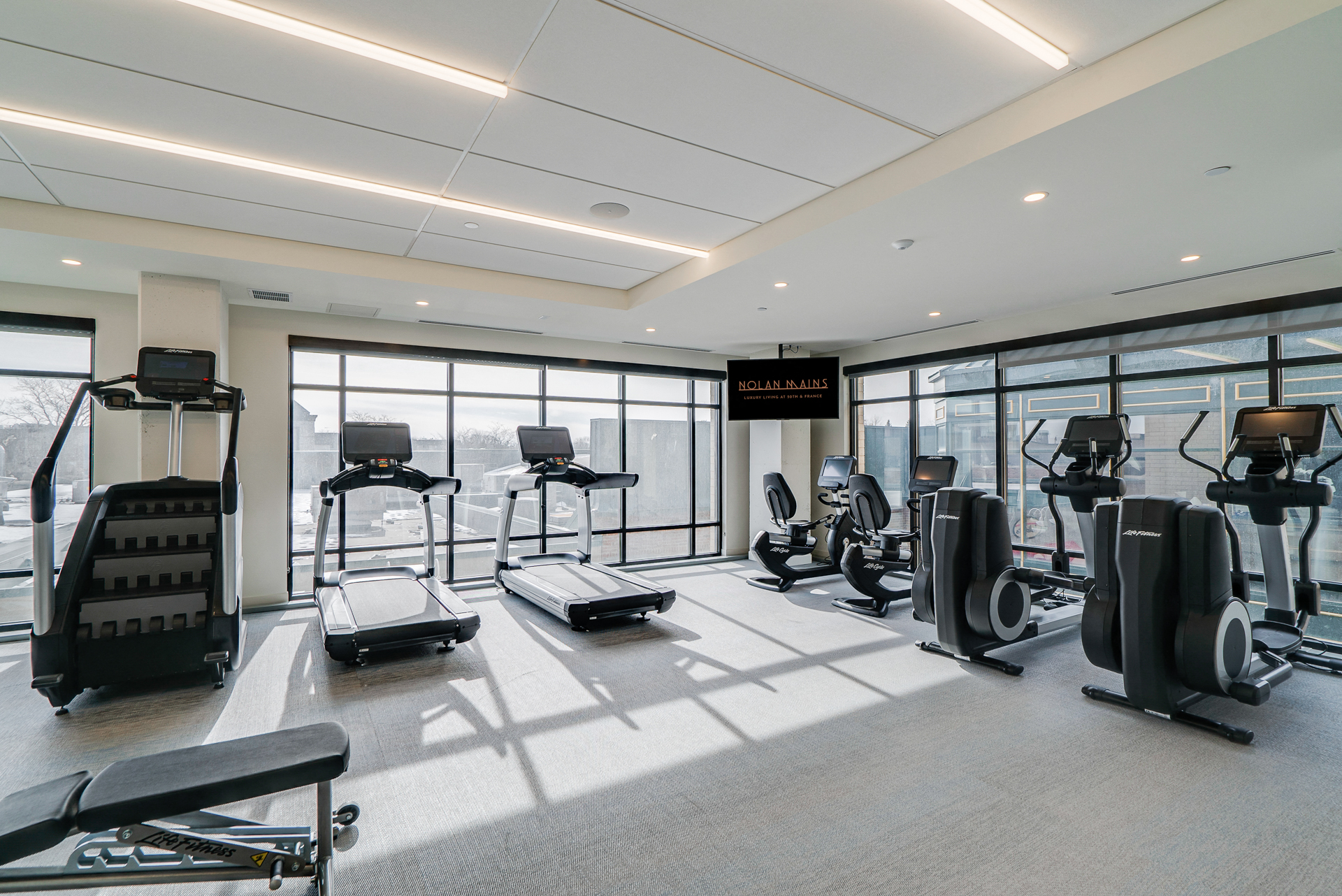 a gym with lots of exercise equipment and floor to ceiling windows