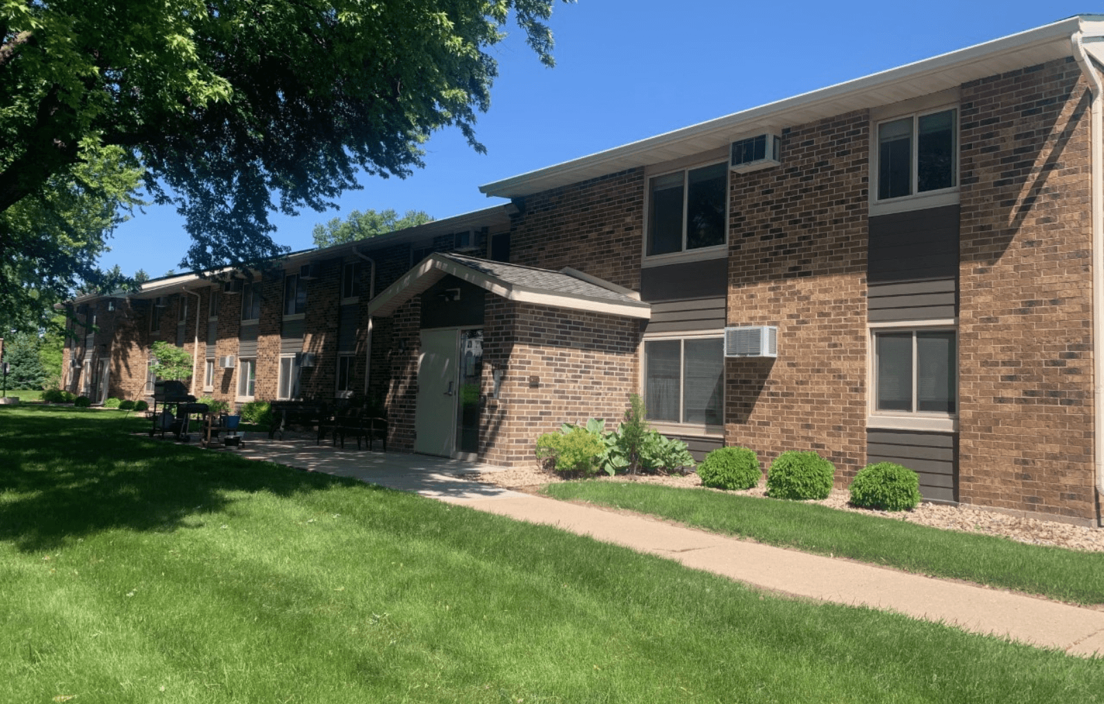 a brick apartment building with a lawn and a sidewalk