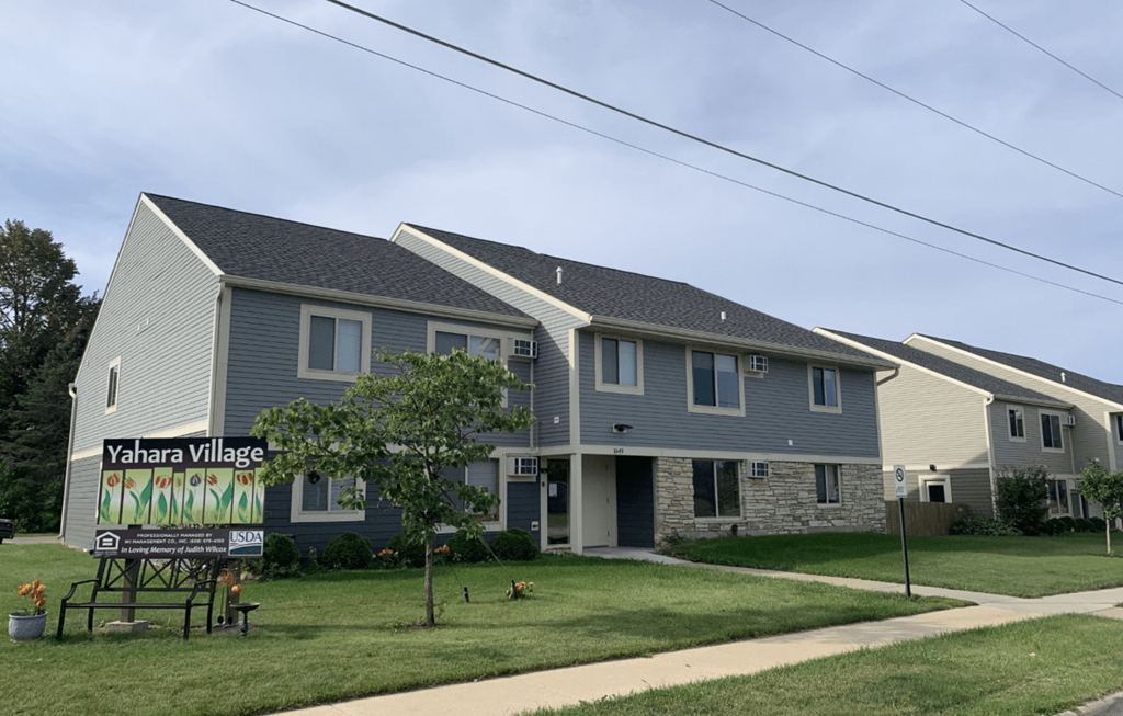 a gray house with a yard sign in front of it
